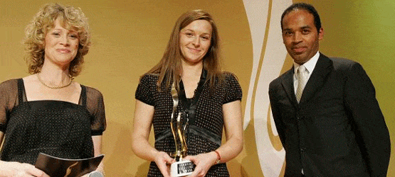 2007 Drei Personen auf einer Bühne, eine Frau hält einen Preis, die anderen beiden stehen daneben und lächeln.