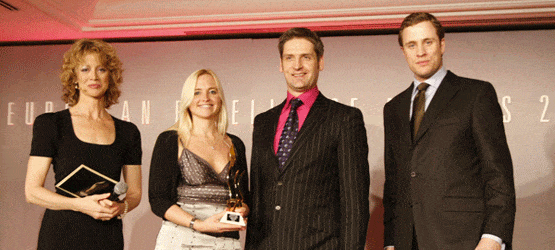 2008 Vier Personen stehen auf einer Bühne, eine Frau hält einen Preis, während die anderen applaudieren. Hintergrund mit Sch...