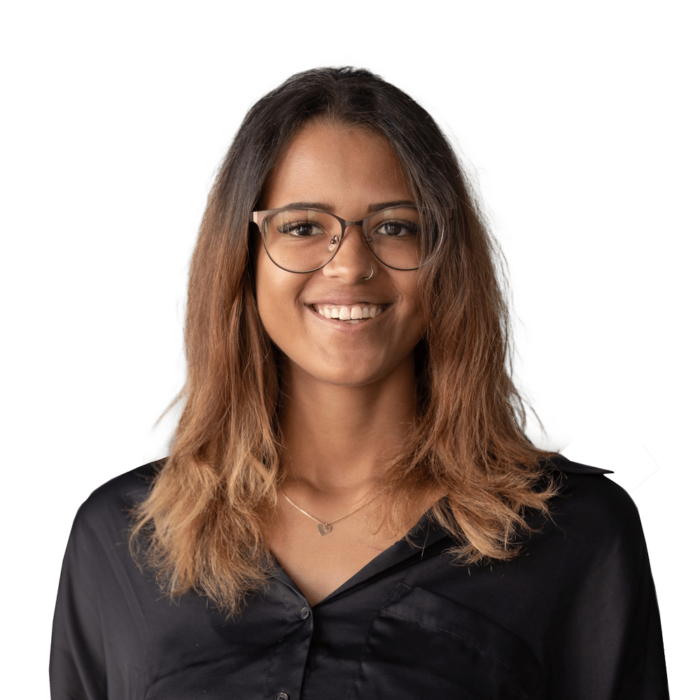 pyritz-cheila Junge Frau mit Brille und langen, lockigen Haaren, lächelt vor grünem Hintergrund. Sie trägt ein schwarzes Hemd.