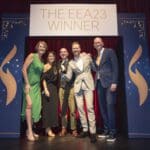 Fünf Personen posieren vor einem Banner mit der Aufschrift "THE EEA23 WINNER" auf einer Bühne.