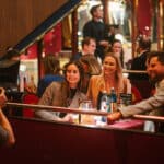 Drei Personen posieren lächelnd an einem Tisch in einem eleganten Restaurant, während ein Fotograf sie aufnimmt.