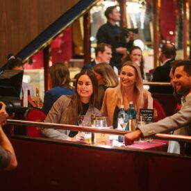 Drei Personen posieren lächelnd an einem Tisch in einem eleganten Restaurant, während ein Fotograf sie aufnimmt.