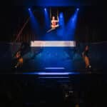 Eine Akrobatin schwingt an einem Seil über einer Bühne mit blauen Lichtern und einem Banner für die European Excellence...