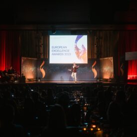 Bühne mit Redner bei den European Excellence Awards 2023, umgeben von Publikum und festlicher Beleuchtung.