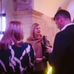 Drei Personen unterhalten sich in einem beleuchteten, modernen Raum mit sanften Farben und architektonischen Details.