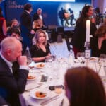 Elegantes Event mit Gästen an Tischen, einem Musiker im Hintergrund und festlicher Atmosphäre.