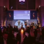 Männer auf Bühne bei der European Excellence Awards 2004, Gäste an Tischen, festliche Atmosphäre mit Kerzenlicht.