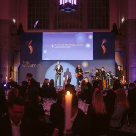Männer auf Bühne bei der European Excellence Awards 2004, Gäste an Tischen, festliche Atmosphäre mit Kerzenlicht.