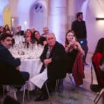 Eine Gruppe von Menschen in eleganter Kleidung sitzt an Tischen bei einer Veranstaltung, mit Kerzenlicht und festlicher De...