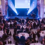 Elegante Preisverleihung mit Gästen an runden Tischen, Bühne im Hintergrund, beleuchtet von blauen Lichtern.