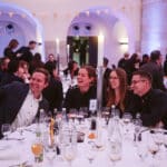 Vier Personen machen ein Selfie an einem festlich gedeckten Tisch in einem lebhaften Veranstaltungsraum.