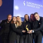Sechs Personen in schwarzer Kleidung halten einen Preis bei den European Excellence Awards 2024 auf einer Bühne.