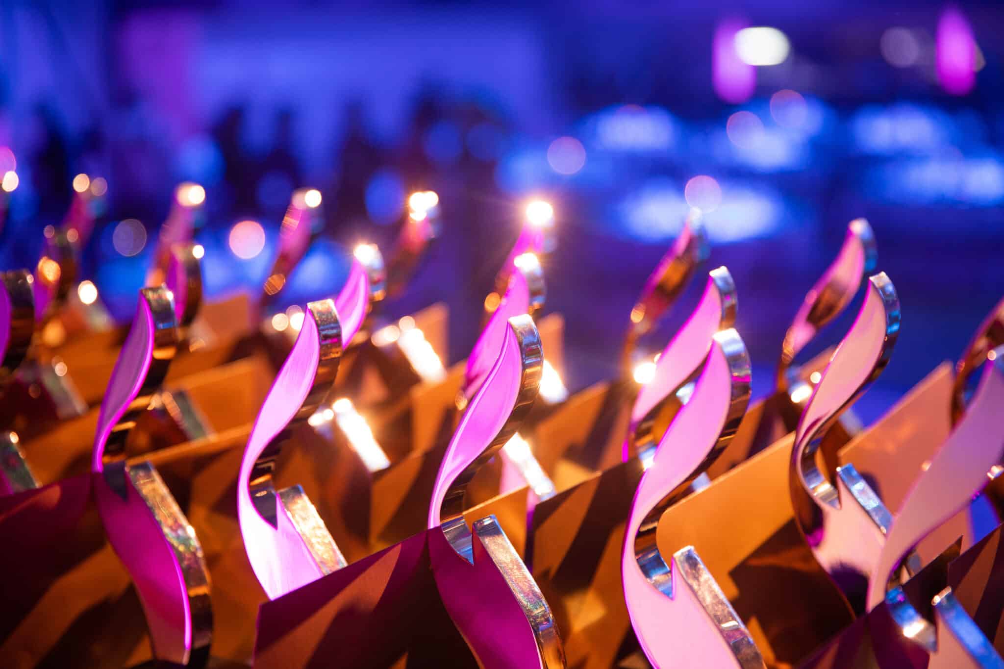 2018-12-06-european-excellence-awards-impressionen-jl-5 Nahaufnahme von glänzenden Auszeichnungen mit lila Beleuchtung im Hintergrund.