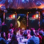 Elegante Award-Show mit festlich dekorierten Tischen, Publikum und großen Bildschirmen im Hintergrund.