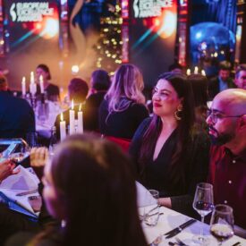 Elegante Award-Show mit Gästen an festlich gedeckten Tischen, Kerzenlicht und festlicher Dekoration im Hintergrund.