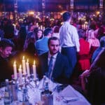 Elegante Award-Show mit Gästen an festlich gedeckten Tischen, Kerzenlicht und farbigem Lichtspiel im Hintergrund.