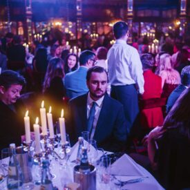 Elegante Award-Show mit Gästen an festlich gedeckten Tischen, Kerzenlicht und farbigem Lichtspiel im Hintergrund.