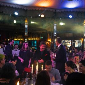 Menschen in formeller Kleidung feiern in einem festlich beleuchteten Saal mit Kerzen auf den Tischen.