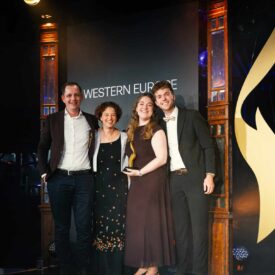 Vier Personen stehen auf einer Bühne vor einem Banner mit der Aufschrift "WESTERN EUROPE" und halten eine Auszeichnung.