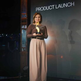 Frau mit braunem Oberteil und beigen Hosen hält einen Preis bei einer Produktlaunch-Veranstaltung.