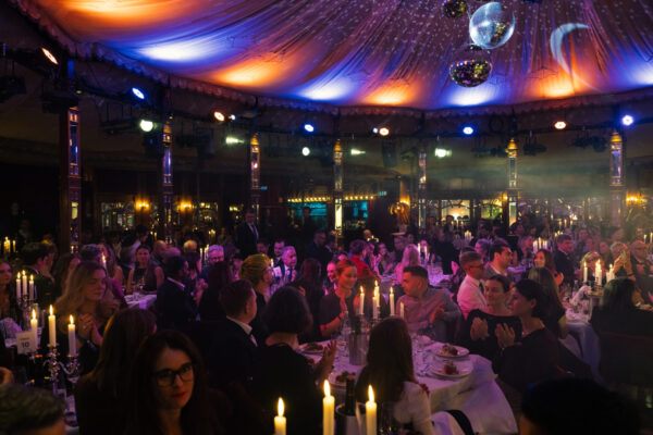 Elegante Award-Show mit festlich gedeckten Tischen, Kerzenlicht und einer bunten Decke aus Lichtern und Spiegeln.