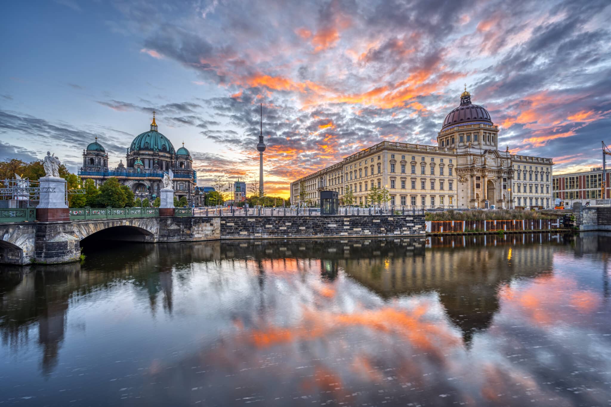 The Berlin City Palace with the Television Tower and the cathedral Berlin City Palace und Fernsehturm spiegeln sich im Wasser bei Sonnenuntergang, umgeben von dramatischem Himmel.