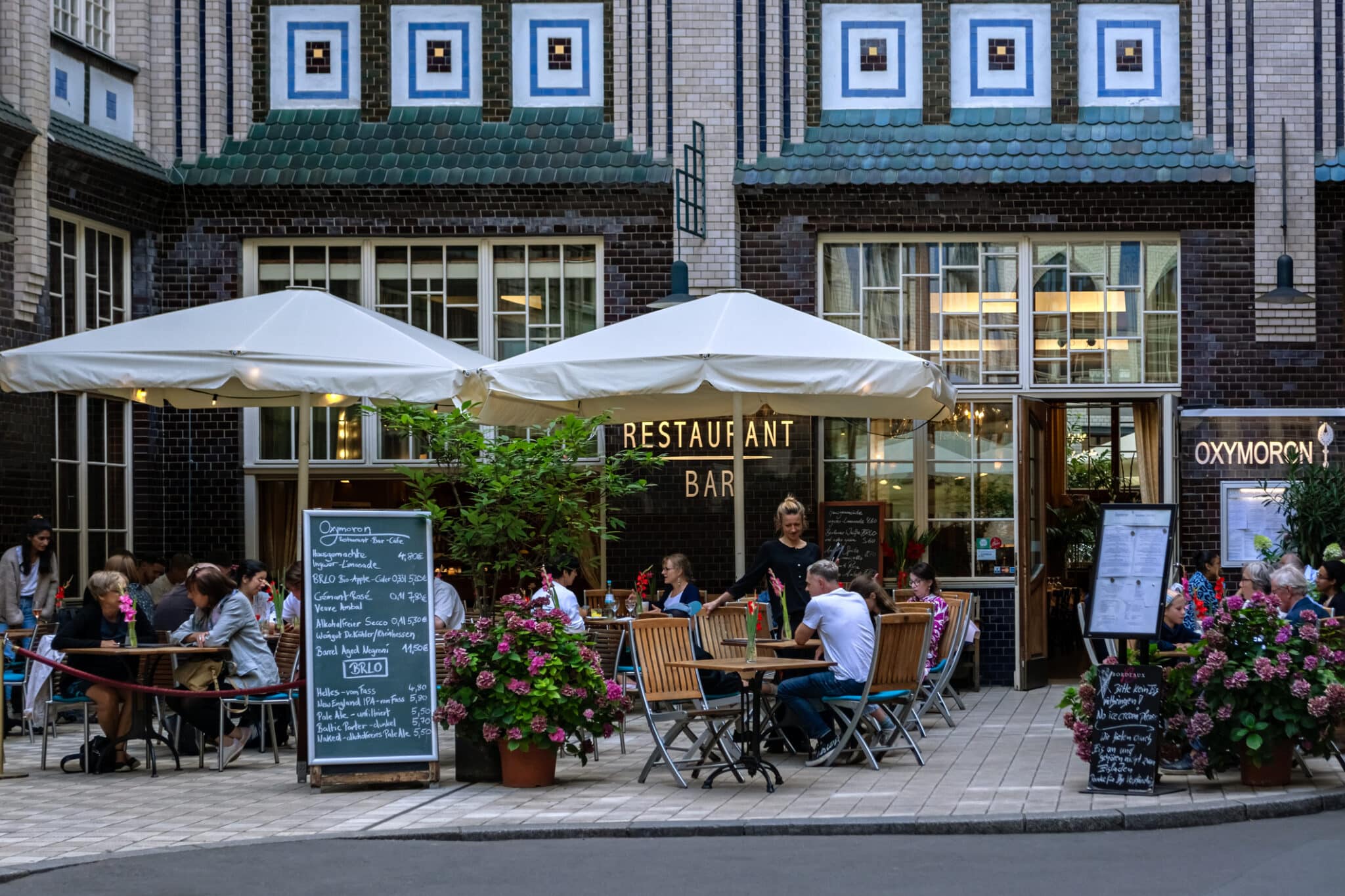 Restaurant in the courtyard of Berlin Gemütliches Restaurant mit Außenbereich, Tischen und Gästen, umgeben von Pflanzen und einer historischen Gebäudefassad...